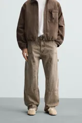 Pantalón gris de corte relaxed fit, con cinco bolsillos, efecto lavado, aplicación de tira y bolsillo multifunción en perneras. Cierre frontal con cremallera y botón.