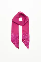 Pañuelo tipo corbatín, largo y angosto, confeccionado en símil seda color fucsia de caída liviana y textura delicada. Su diseño presenta detalles de lentejuelas bordadas en los extremos.