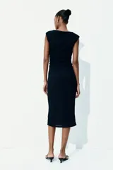 Vestido midi negro de punto arrugado con mangas japonesas y escote barco. Diseño ajustado con laterales fruncidos para un efecto drapeado que realza la figura.