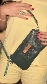 Mini cartera de cuero color verde oscuro con textura craquelada, cierre superior con cremallera y correa larga desmontable.