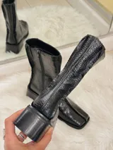 Bota negra de caña media con textura de cocodrilo, punta cuadrada y tacón bajo.