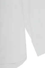 Camisa blanca de popelina de algodón, de corte amplio, manga larga, cuello clásico, cierre frontal con botones y puños abotonados.