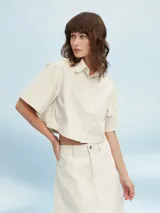 Camisa de denim celeste con corte cropped, mangas cortas y bolsillo en el pecho.