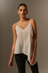 Blusa blanca de poliéster con breteles finos, escote en V, corte asimétrico y volados.