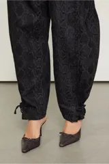 Pantalón negro con estampado de piel de serpiente, de tiro bajo y corte holgado, con puños ajustables con lazos.