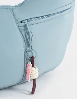 Cartera saca negra de tela deportiva con correa regulable, cierre superior y bolsillo frontal con cierre. Incluye charm lateral.