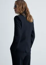 Blazer negro con raya diplomática, cuello de pico con solapa, cierre de botones en la parte delantera, manga larga con puños abotonados, diseño recto y estructurado, un bolsillo de ribete en el pecho y dos bolsillos de ribete con solapa laterales.