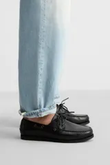 Zapato náutico de cuero negro con cordones de cuero y suela plana.