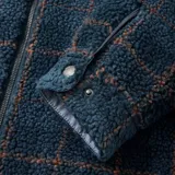 Campera tipo camisa de sherpa azul con diseño a cuadros marrones, cierre frontal con cremallera, cuello clásico y dos bolsillos con solapa abotonada en el pecho.