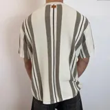 Remera de punto calado color blanco con rayas verticales marrones y negras, corte holgado y mangas cortas.