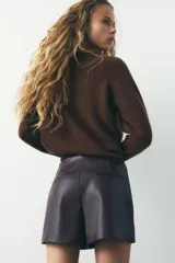 Falda pantalón corta marrón de tiro medio con efecto piel, falsos bolsillos de vivo en la espalda y cierre lateral con cremallera oculta.
