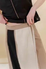 Falda midi de lino y algodón con paneles verticales en color beige, negro y tostado. Diseño portafolio con cruce, abrochada con botones y broches de presión regulables. Detalles desflecados en los cortes verticales y bolsillo escondido en el lateral derecho.