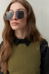 Vestido corto de algodón color verde oliva, de corte recto, con cuello redondo y apliques metálicos en el escote y sisas. Se lleva sobre una camisa negra de manga larga.