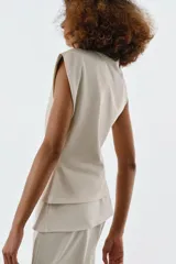 Top de algodón color beige, con cuello recto, mangas asimétricas y detalle de tejido drapeado en el lateral.