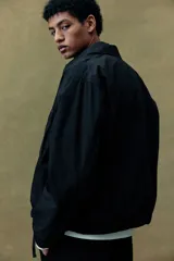 Campera negra con cuello camisero, cierre frontal y bolsillos superiores con solapa. Elástico revestido en puños y bajo.