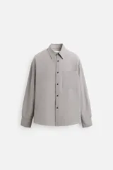 Camisa de hombre relaxed fit con cuello solapa, manga larga con puño abotonado, bolsillo de parche en el pecho y cierre frontal con botones. Diseño a cuadros en tonos gris y blanco.