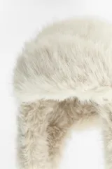 Gorro tipo aviador color crema confeccionado en tejido de pelo sintético. Forro interior combinado a tono. Cierre ajustable con lazada.