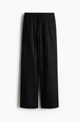 Pantalón negro de corte holgado en algodón, con tiro alto, cintura elástica fruncida y cordón para ajustar. Piernas anchas con bolsillos laterales.