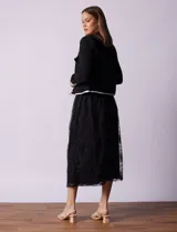 Chaqueta de tweed blanca con ribete negro, escote a la base, abertura central con botones, bolsillos delanteros y puños con aplique de botones perlados.