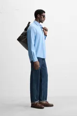 Camisa celeste de lyocell y algodón, corte relaxed fit, cuello solapa, manga larga con puños abotonados, bolsillo de parche en el pecho y cierre frontal con botones.
