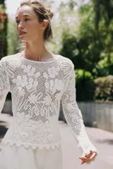 Top blanco de encaje con bordados florales, cuello redondo y mangas largas.