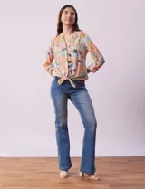 Blusa de gasa estampada a rayas verticales en tonos celeste, lila, naranja y marrón. Tiene cuello a la base con escote en V y botones. Delantera con bolsillo aplicado. Largo de manga regulable con presilla y botón. Terminación anudada opcional.