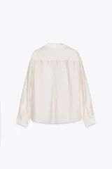 Camisa color crudo confeccionada en lyocell. Tiene cuello solapa, manga larga con puños y cierre frontal con botones. Cuenta con un bolsillo de plastrón con bordados a tono en el pecho.