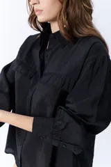 Camisa negra de manga larga con cuello clásico, cierre frontal con botones y dos bolsillos con solapa en el pecho.