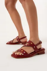 Sandalia baja color rojo de cuero con agarre trasero con hebilla y detalle de tachas de distintas medidas en la capellada.