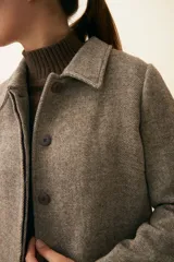 Tapado largo con cuello solapa y corte recto, color gris claro. Tiene cierre frontal con botones ocultos, tajos laterales y bolsillos escondidos en el corte lateral. Está forrado y confeccionado en lana fina sin teñir, diseñada exclusivamente por Don Baez. Hecho 100% en Uruguay.