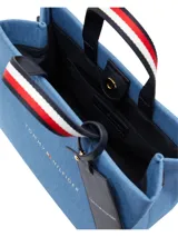 Cartera Tommy Hilfiger tipo shopper tote de tamaño mediano, confeccionada en poliéster con diseño denim azul. Tiene doble asa superior con detalle de rayas rojas, blancas y azules, correa de hombro ajustable y extraíble, cierre principal y bolsillo interno. Incluye llavero colgante con logo de la marca.