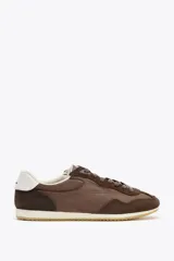 Zapatillas deportivas marrones con detalles en gamuza, cordones marrones y suela blanca.