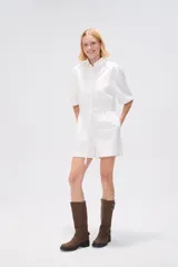 Mono corto blanco de algodón, con cuello camisero, cierre frontal con botones, mangas cortas y bolsillos.