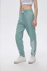 Pantalón de jogging color celeste con cintura elástica ajustable con cordón y puños elásticos. Presenta tres tiras verticales blancas en la parte inferior de la pierna.