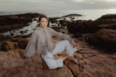 Blusa color gris con estampado floral blanco, cuello mao con lazo, mangas largas abullonadas con puños elásticos.