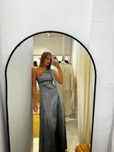 Vestido largo de tafeta con brillo, color gris o plateado, con escote asimétrico de un solo hombro y una pieza de seda liviana que cae como una capa o chal.