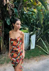 Vestido midi con estampado tie-dye en tonos rosados, azules y beige. Tiene escote drapeado, breteles finos y falda irregular con abertura lateral.