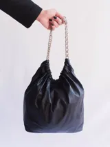 Bolso negro de cuero con fruncido superior y asas de cadena plateada.
