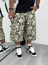Pantalón ancho de estilo cargo con estampado camuflado en tonos verde oliva, beige y blanco. Presenta cierres a la altura de la rodilla que permiten convertirlo en short.