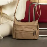 Bandolera color beige de símil cuero con dos bolsillos frontales con cierre, doble apertura superior con cierre, un bolsillo trasero con cierre y dos bolsillos internos. Incluye correa de galón larga regulable para llevar al hombro.