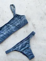 Conjunto de bikini con estampado geométrico en tonos celeste, azul, blanco, amarillo y naranja. El corpiño es bandeau con breteles regulables y lazo en la espalda. La bombacha es vedetina con frunce elástico en los costados.