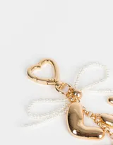 Llavero con dije de letras doradas que forman la palabra "LUCK" y cinta de perlas sintéticas.