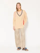 Sweater beige de punto con cuello en V con rayas azul marino y tiras trenzadas rojas y rosas en los laterales.