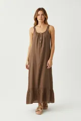 Vestido largo sin mangas color marrón, con escote redondo fruncido y botones frontales. Presenta tirantes anchos con detalle de tejido trenzado y un volante con encaje en el ruedo.