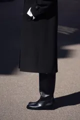 Abrigo negro de cuello solapa y manga larga con trabilla y botón. Tiene bolsillos delanteros de vivo y cierre frontal cruzado con botones.