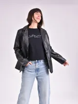 Chaqueta negra de cuero sintético, con cuello clásico, solapas y cierre frontal con un botón.