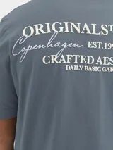 Remera azul de manga corta con cuello redondo y estampado en la espalda con la frase "ORIGINALS STUDIO Copenhagen EST.1990 Workshop CRAFTED AESTHETICS DAILY BASIC GARMENTS".