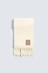 Bufanda color crema confeccionada en tejido con lana y acabado cepillado. Tiene flecos en los extremos.