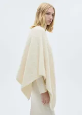 Poncho de punto color crudo, con cuello redondo y bajo asimétrico. Tejido con lana, poliéster y acrílico.