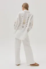 Camisa blanca de lino con bordados florales en tonos dorados y marrones en el frente y las mangas.